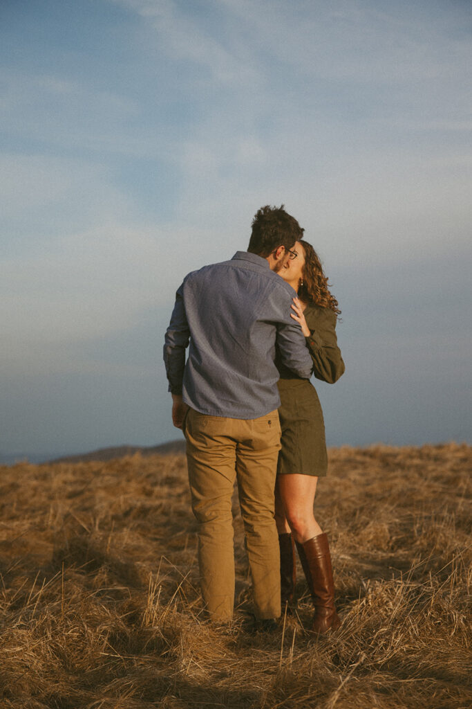 Man and woman cuddling and kissing during engagement photos at Max Patch mountain in North Carolina.