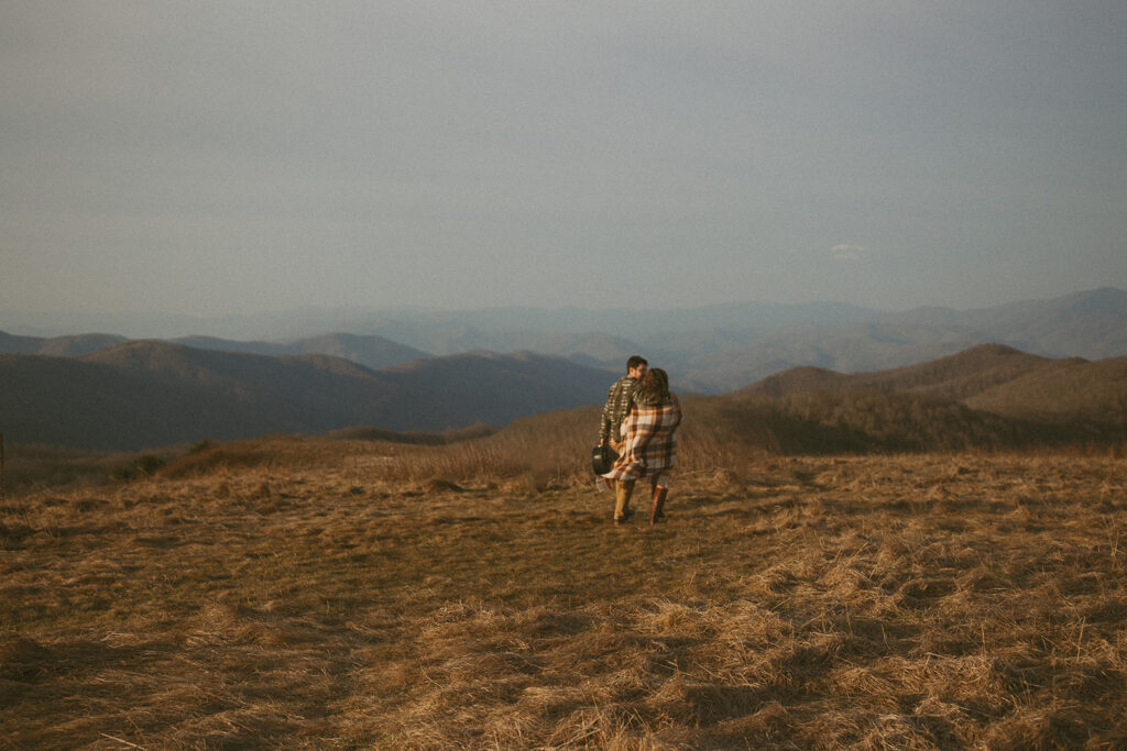 Man and woman walking away and looking at each other during engagement photos at Max Patch mountain in North Carolina.