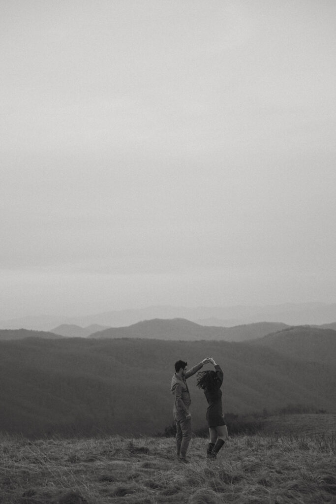 Man spinning woman during engagement photos at Max Patch mountain in North Carolina.