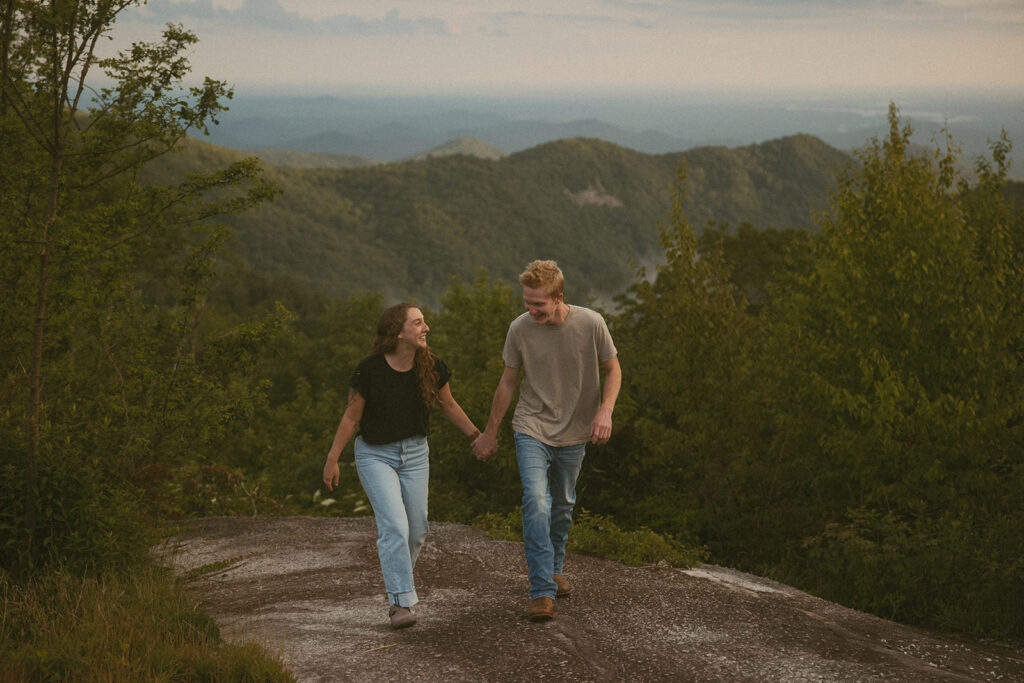 Man and woman holding hands and laughing while standing on a rock at Sassafras Mountain.