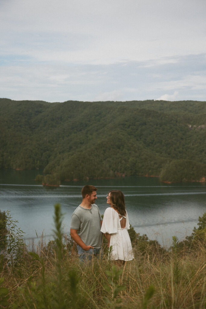 man and woman smiling at each other with mountains behind them
