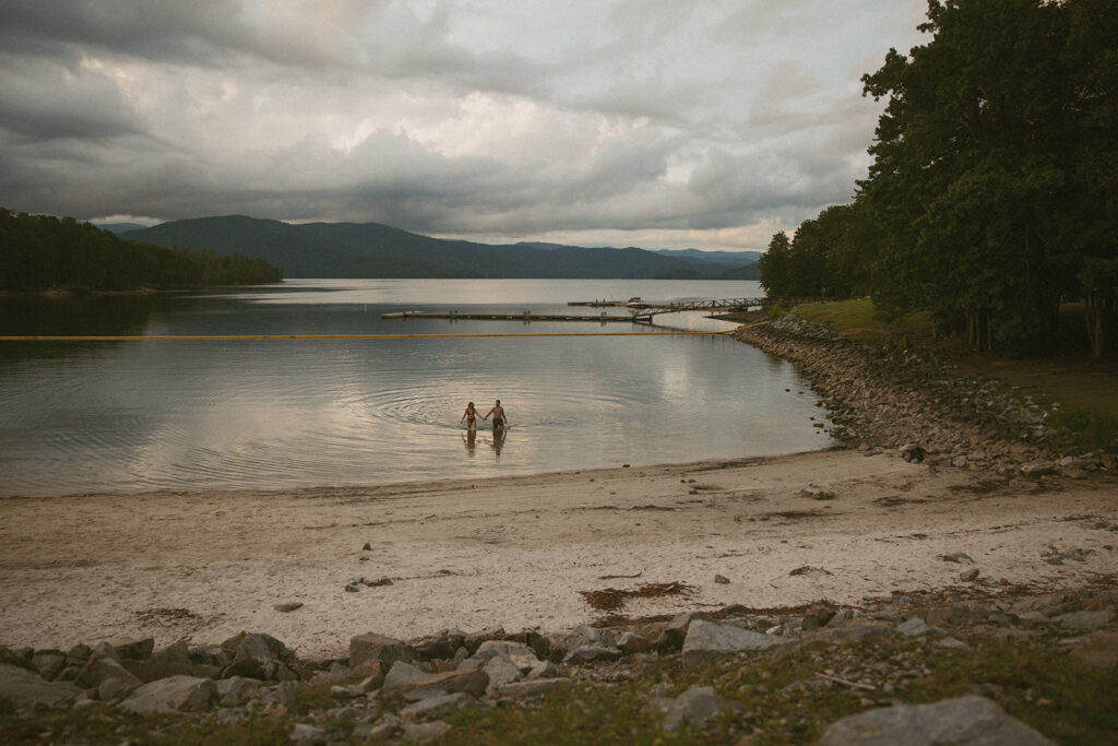 man and woman holding hands wearing swimsuits walking out of water with mountain behind them