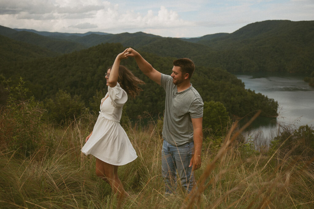 man spinning woman in the grass with mountains behind them