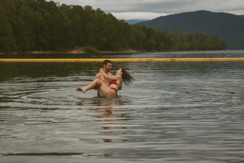 man spinning woman in the lake with mountains behind them 