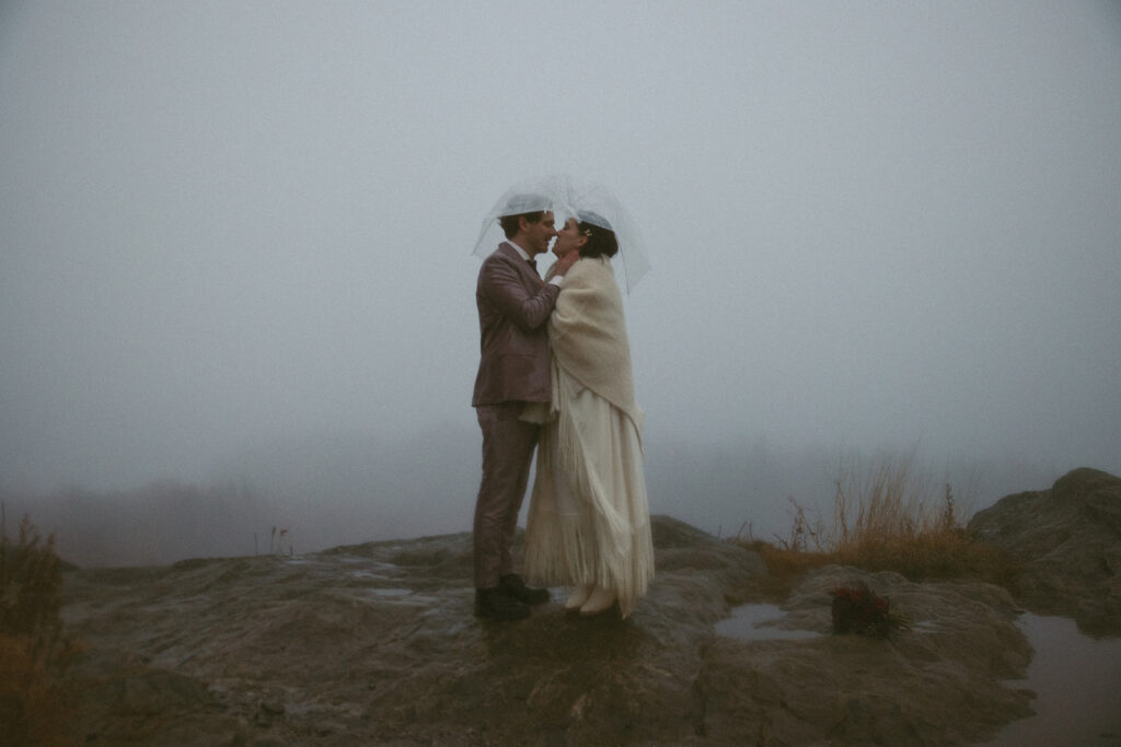 man and woman under the same umbrella about to kiss during their rainy day elopement