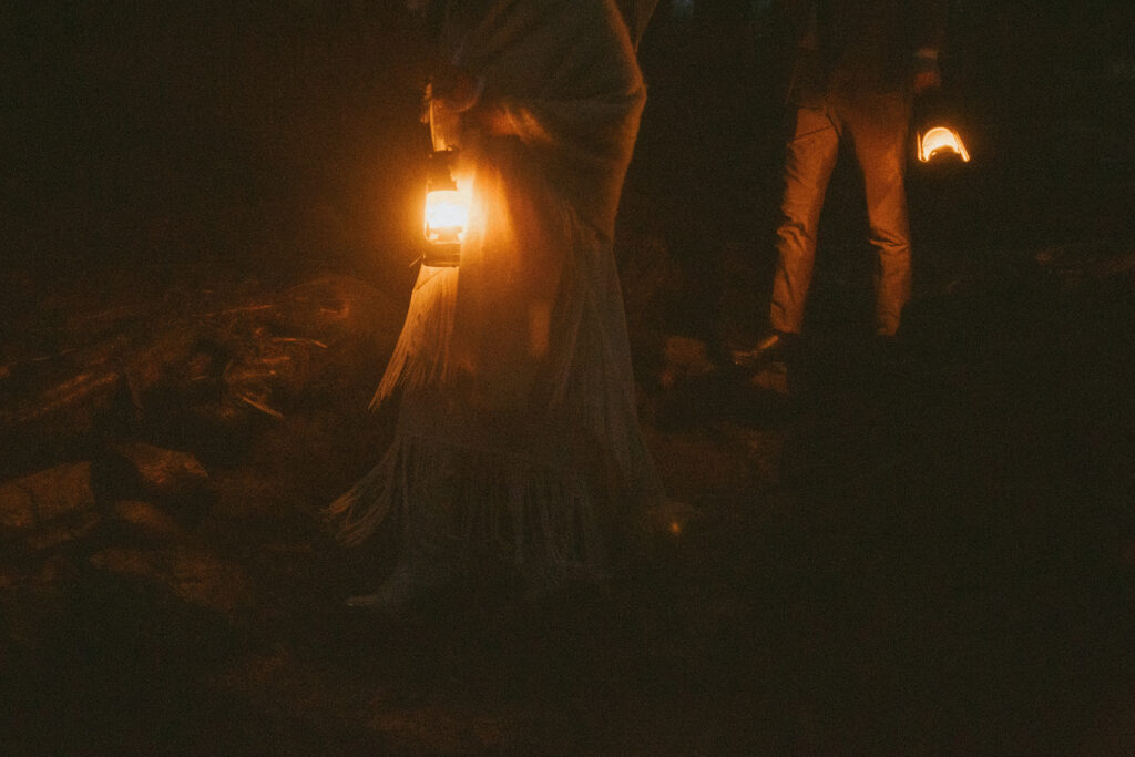 man and woman holding lanterns while they hike down mountain after elopement