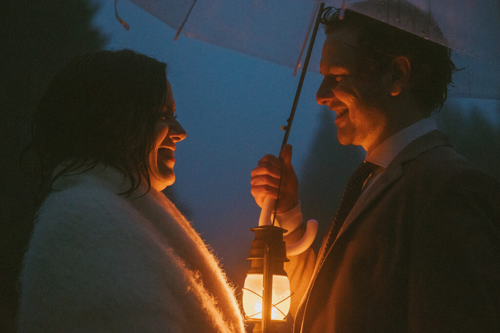 man and woman standing underneath umbrella on the road holding lanterns on their elopement day