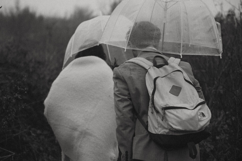 man and woman hiking with umbrellas during their rainy day elopement