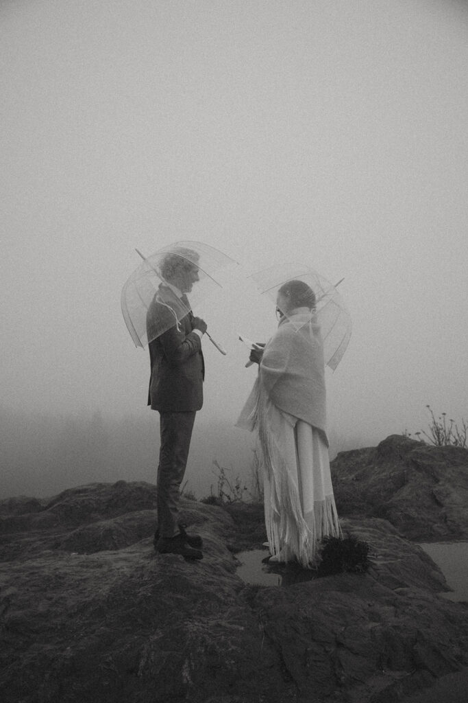 man and woman exchanging vows on a mountain top during their rainy day elopement