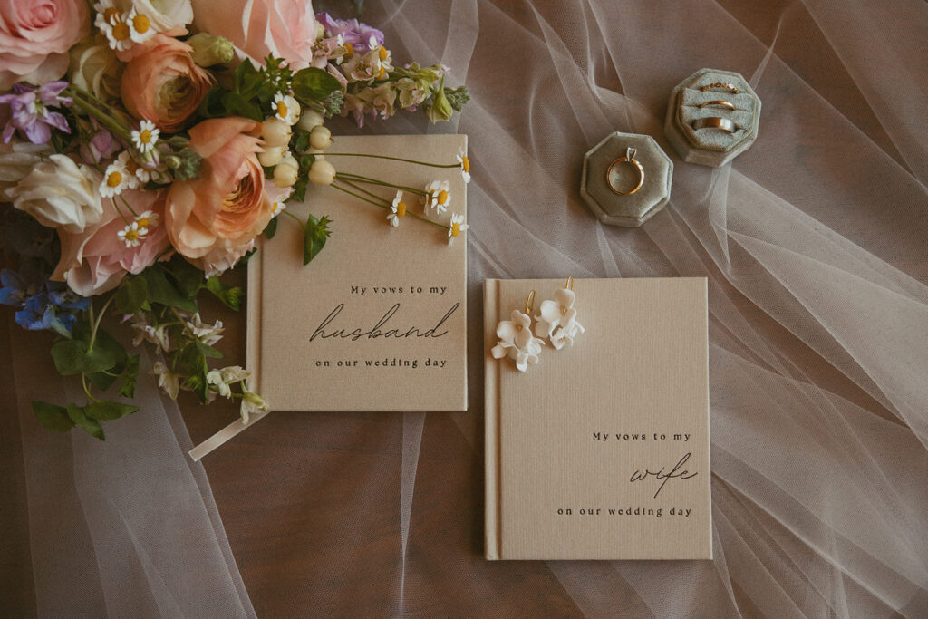 husband and wife vow books in a flat lay with their wedding rings and flowers