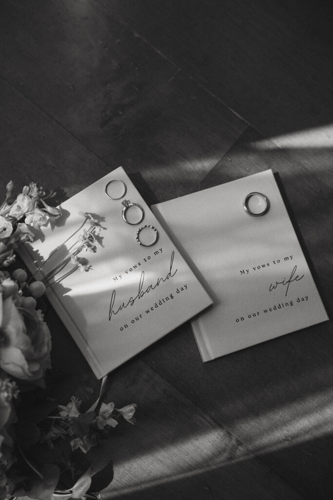 husband and wife vow books with their rings and flowers in a flat lay