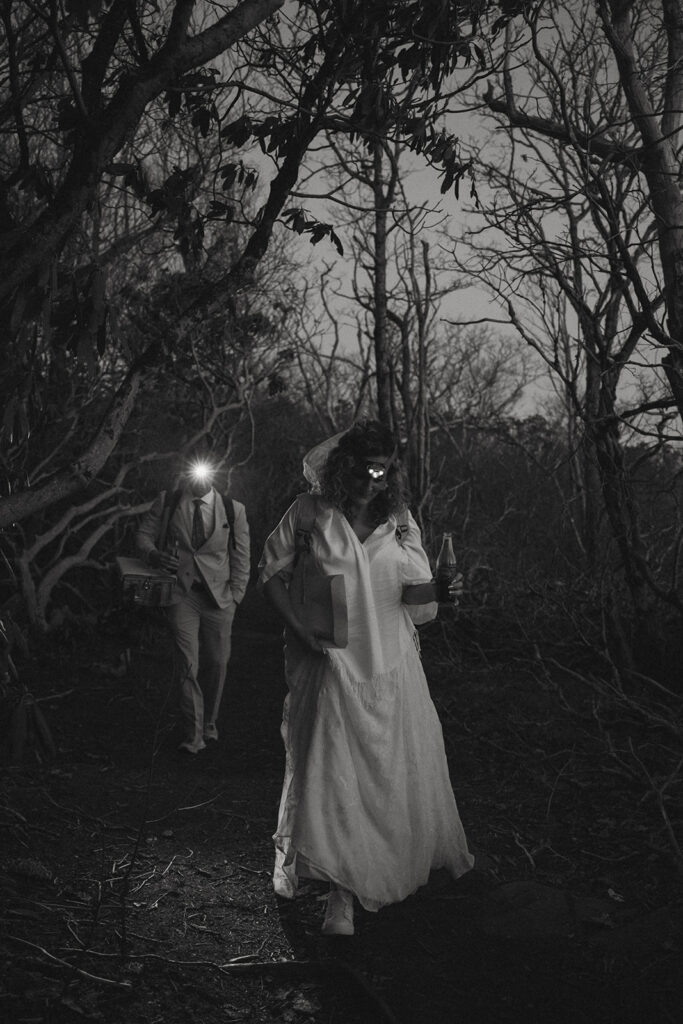 Man and woman in wedding attire hiking down trail after dark with their headlamps