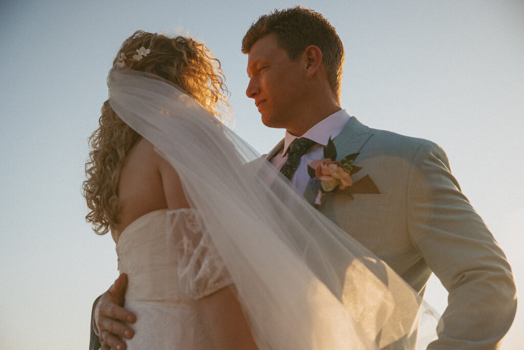 man and woman in wedding attire holding each other with nothing but sky behind them