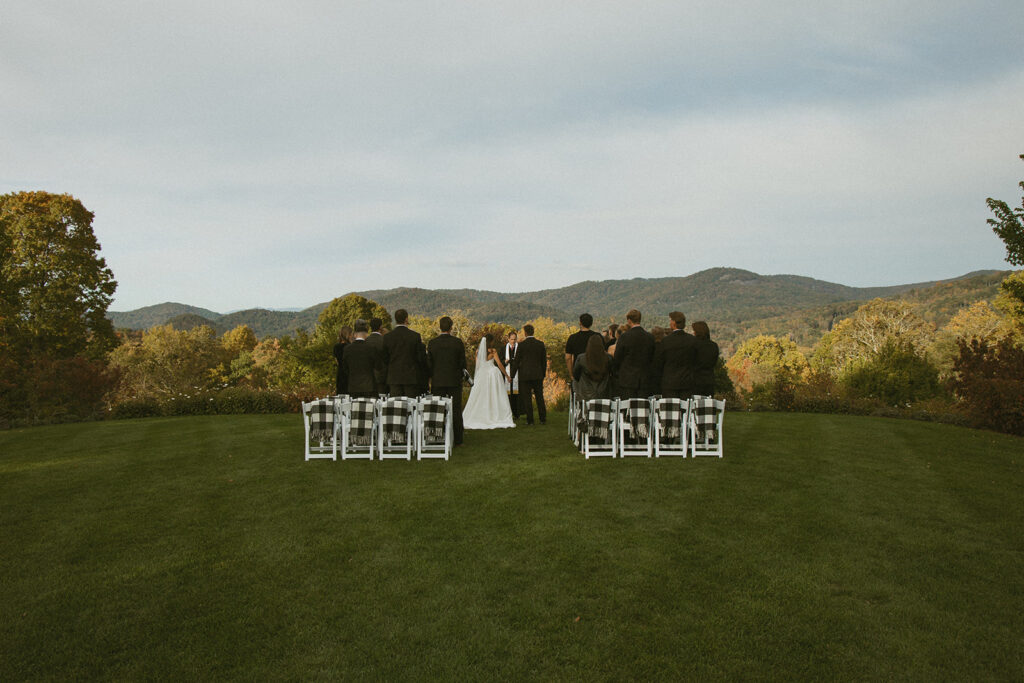 a small wedding ceremony on lawn with mountains in front of them