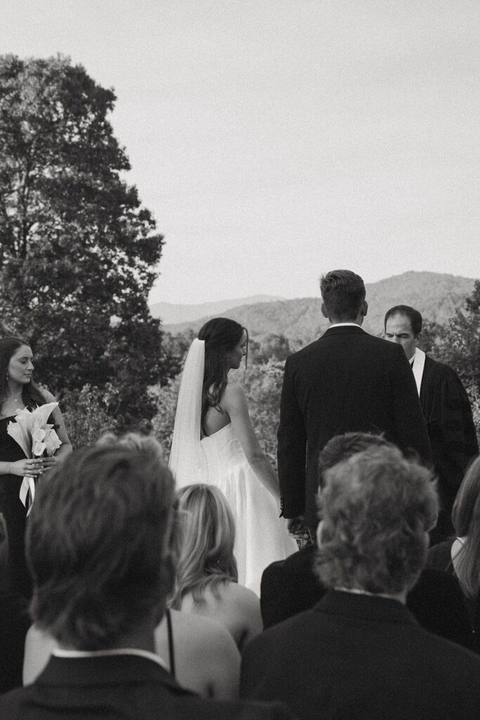 husband and wife standing at wedding ceremony with guests watching