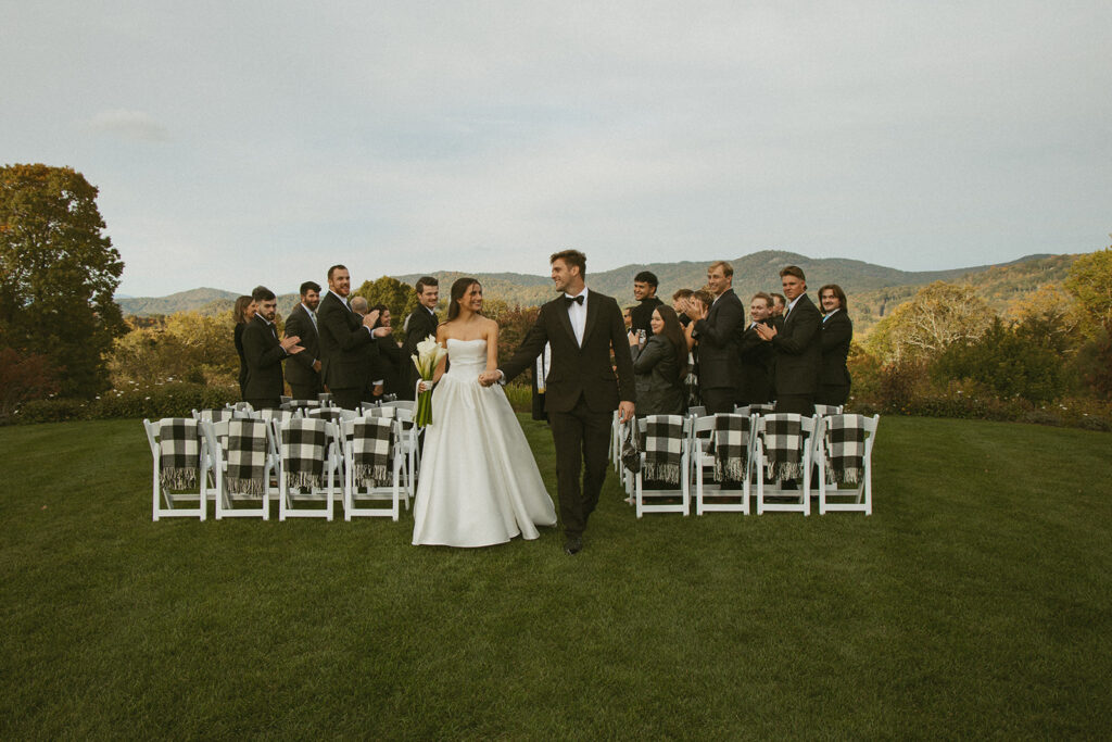 Husband and wife walking back down aisle after wedding with their guests clapping and the mountains behind them
