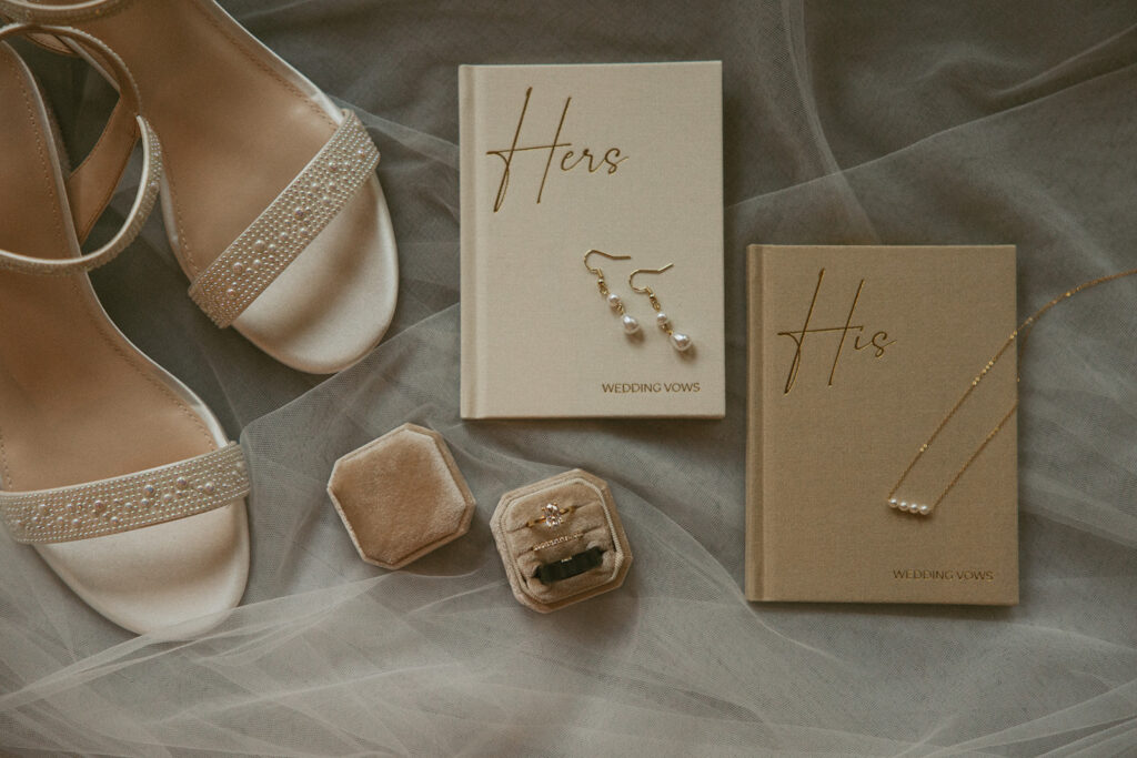 his and her vow books laying with rings, earrings and shoes