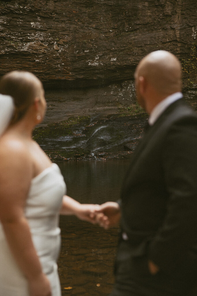 man and woman in wedding attire standing on rocks and looking at cherokee falls in cloudland canyon