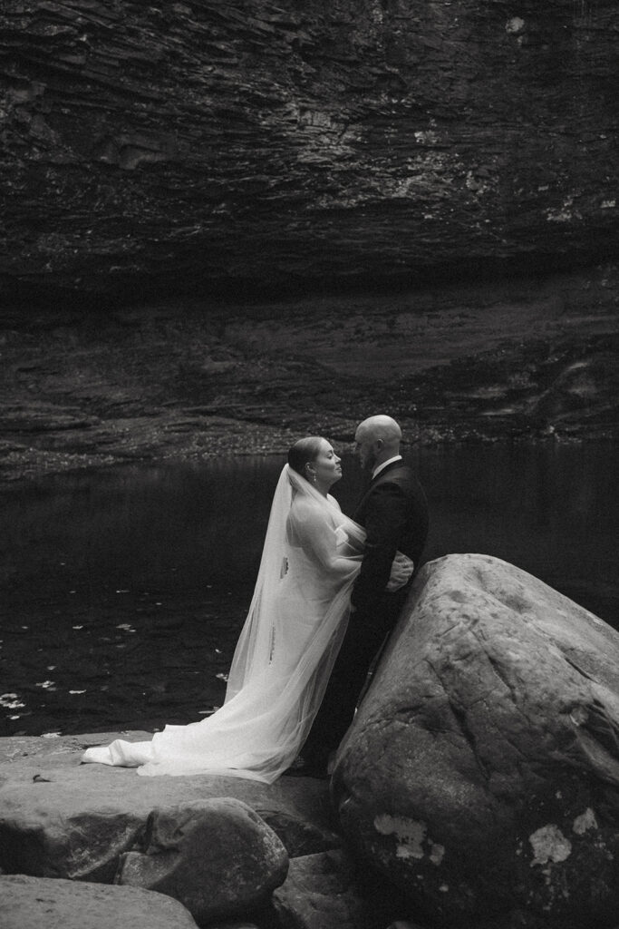 man and woman in wedding attire standing on rocks and looking at cherokee falls in cloudland canyon