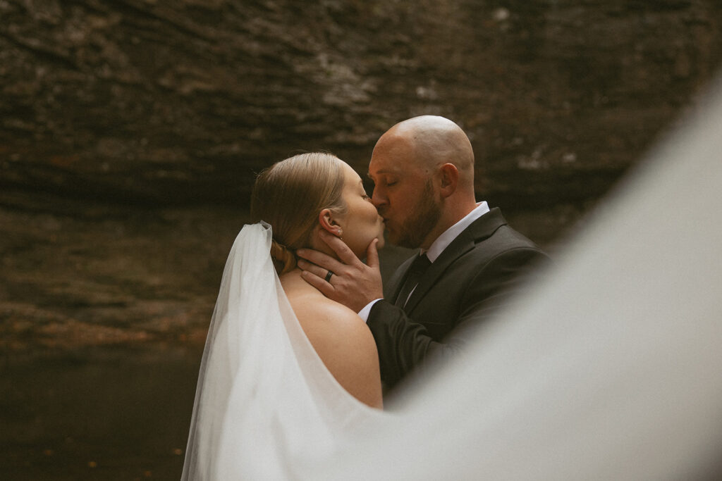 man and woman in wedding attire kissing at cherokee falls in cloudland canyon