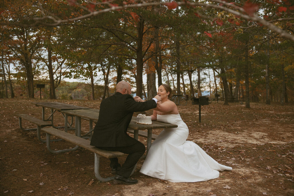 man and woman sitting at picnic table feeding each other cake during their elopement