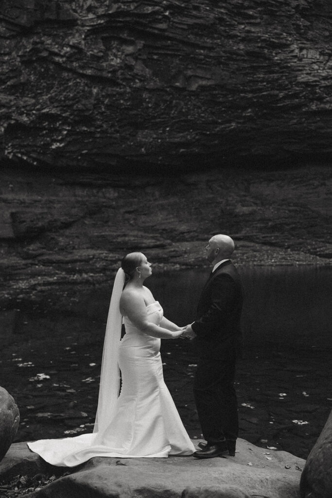 man and woman in wedding attire standing on rocks at cherokee falls in cloudland canyon